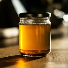 Słoik złocistego miodu na drewnianym stole. Czy miód nawilża gardło? Ten naturalny produkt może przynieść ulgę.