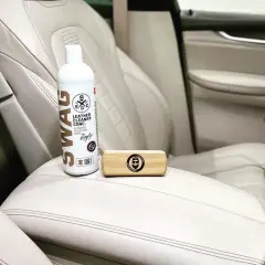 Zestaw do pielęgnacji jasnej skóry w aucie: butelka z preparatem SWAG Leather Cleaner i drewniana szczotka. Idealne rozwiązanie, czym czyścić skórę w aucie.