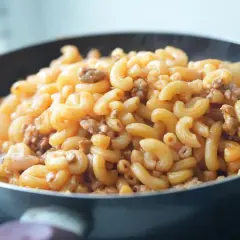 Gorący makaron z mięsem mielonym w sosie, parujący w patelni. Pyszne danie gotowe do podania.