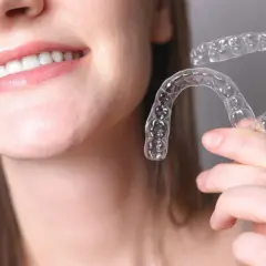 Una persona sonríe mostrando sus dientes y sostiene un alineador transparente. Invisalign para que sirve: para corregir la alineación dental de forma discreta.