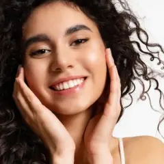Sonrisa radiante con un toque de strawberry makeup, cabello rizado oscuro y piel luminosa.