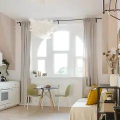 Jasne, przytulne mieszkanie idealne na najem okazjonalny. Biała kuchnia, okno z zasłonami, stolik z krzesłami i wygodna sofa.