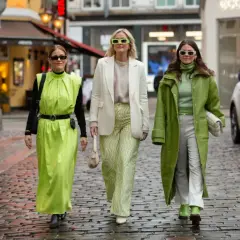 Tre kvinnor i ljusgröna och vita kläder, med solglasögon, promenerar på en kullerstensgata. En tydlig dansk kvinna stil.