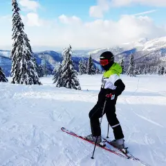 Narciarz na łagodnych stokach narciarskich Zakopane dla początkujących, otoczony ośnieżonymi drzewami i górami.