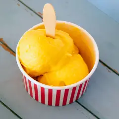 Un refrescante helado de mango en un recipiente a rayas rojas y blancas, listo para disfrutar en un día caluroso.