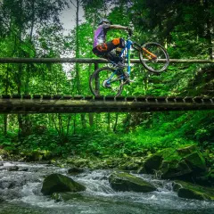 Rowerzysta wykonuje trik na drewnianym moście nad potokiem. Wspaniałe **trasy rowerowe Zakopane** czekają na odkrycie!
