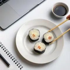 Praca i zdrowie idą w parze. Na biurku laptop, notatnik i pałeczki do sushi, idealne dla zwolenników peskatarianizmu.