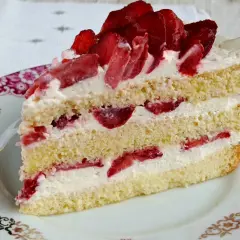 Pyszny tort z bitą śmietaną i truskawkami, przełożony kremem i owocami, na ozdobnym talerzyku.