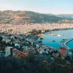 Widok na zatokę i miasto Alanya, z górami w tle. Widać port z łodziami i charakterystyczną czerwoną wieżę, część historycznego Alanya stare miasto.
