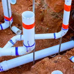 Prace hydrauliczne w toku: łączenie rur pcv w wykopie. Widać fragmenty instalacji kanalizacyjnej i drenażowej.