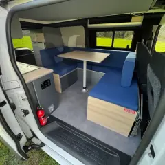 Aménagement intérieur d'un camping-car : banquettes bleues, table, coin cuisine. Idéal pour construire son camping car.
