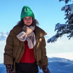 Frau mit grüner Strickmütze und brauner Winterjacke im Schnee.