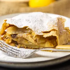 Ein Stück Apfelstrudel, bestäubt mit Puderzucker, wartet auf dem Teller. Dieses Apfelstrudel Rezept ist ein Genuss.
