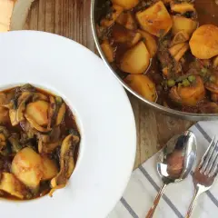 Un plato de papas con choco, un guiso casero con trozos de patata, calamares y guisantes en una salsa oscura.
