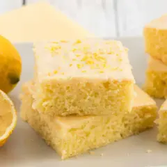 Saftiger Zitronenkuchen vom Blech, bestreut mit Zitronenschale. Daneben liegen frische Zitronen.