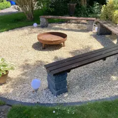Gemütliche Kies Garten Sitzecke mit Feuerstelle und Holzbänken. Kugelleuchten sorgen für stimmungsvolles Licht.