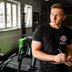 Trener Paweł tworzy spersonalizowany plan treningowy na biceps, notując ćwiczenia na tablicy.