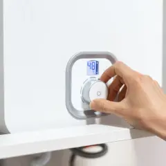 Mano che gira la manopola per spegnere la caldaia a condensazione. Display digitale mostra 48°C.