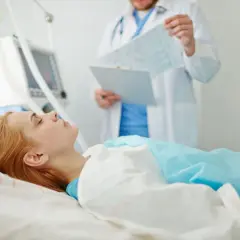 Kobieta w śpiączce leży podłączona do respiratora, lekarz analizuje jej wyniki.