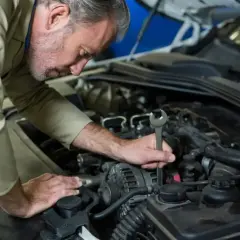 Mechanik z kluczem w ręku sprawdza świece żarowe w silniku samochodu.