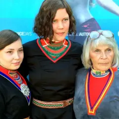 Tre kvinnor i traditionella samiska dräkter poserar framför en blå bakgrund med logotyper. De representerar en stark berättelse, likt den i feministiska filmer.