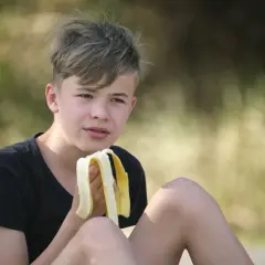 Chłopiec je banana. Zastanawia się, ile kalorii powinna jeść 13 latka, by mieć energię do zabawy.