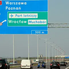 Znak drogowy pokazuje, jak dojechać na lotnisko we Wrocławiu z dworca PKP. Kierunek na lotnisko i Wrocław Muchobór jest po prawej stronie.