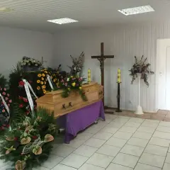 Drewniana trumna otoczona wieńcami i kwiatami, krzyż i świece tworzą najpiękniejsze ostatnie pożegnanie.