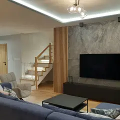 Nowoczesne lamele ścienne aranżacje tworzą ciepłą atmosferę obok kamiennej ściany z TV.