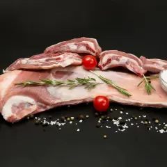 Poitrine d'agneau crue, parsemée de sel, poivre, romarin et tomates cerises, prête à être cuisinée.