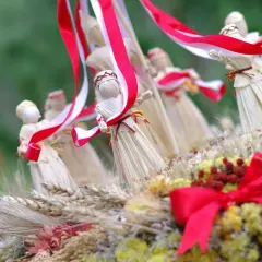 Słomiane figurki, jak posag panny młodej, ozdobione biało-czerwonymi wstążkami, wśród kłosów i suszonych kwiatów.