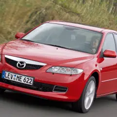 Czerwona Mazda 6 GG w ruchu, z uśmiechniętą kobietą za kierownicą, na tle zieleni.