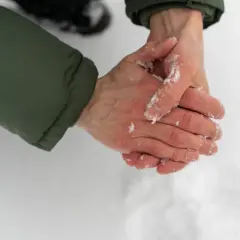 Händer med snö på, som gnuggas mot varandra för att värma upp torra handflator.