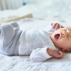 Ein Baby gähnt auf einer Decke mit Sternen. Wann Babys alleine einschlafen, ist eine Frage, die viele Eltern beschäftigt.