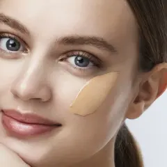 Una donna con un tocco di fondotinta sulla guancia, un esempio visivo di come applicare il fondotinta per un look naturale.