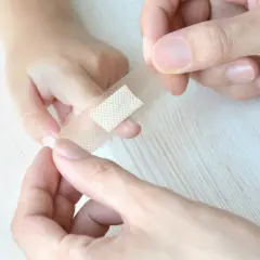 Ręce przyklejają plaster na palec dziecka, by pomóc mu jak oduczyć dziecko ssania palca przy zasypianiu.