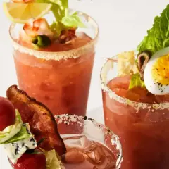 Tre glas med Bloody Mary, dekorerade med räkor, ägg, bacon och grönsaker. En festlig brunchdrink!