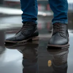 Man in jeans and black boots standing in a puddle. Learn how to rough up the bottom of slippery shoes for better grip.