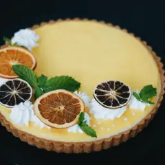Pyszna tarta z owocami: cytrynowy krem, suszone pomarańcze i limonki, listki mięty i ozdobne kleksy bitej śmietany.