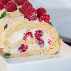 Saftige Biskuitrolle mit frischen Himbeeren und Sahne gefüllt, garniert mit Beeren und Mandelblättchen. Ein Genuss!