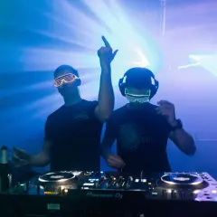 Dwóch DJ-ów w neonowych okularach gra muzykę trance na imprezie z laserami.