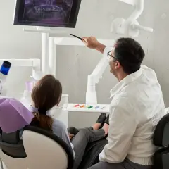 Dentysta omawia z pacjentką zdjęcie RTG, wyjaśniając przebieg leczenia. Ciekawe, ile zarabia dentysta za taką troskę o zdrowie pacjentów.