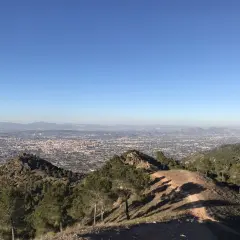 Vista panorámica desde la sierra de carrascoy, con un extenso paisaje urbano y montañas al fondo bajo un cielo azul despejado.
