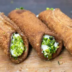 Trzy chrupiące cannoli, jedne z najpopularniejszych dań włoskich, wypełnione kremem i posypane pistacjami.