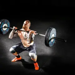 Mężczyzna z tatuażami wykonuje rack pull z ciężarem.