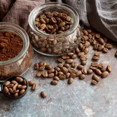 Due barattoli di vetro, uno con caffè macinato e l'altro con caffè in grani, con chicchi sparsi. Quale scegliere per il tuo caffè perfetto?