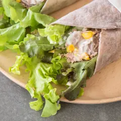 Pyszna tortilla z tuńczykiem, świeżą sałatą i kukurydzą, zawinięta w papier i przewiązana sznurkiem.