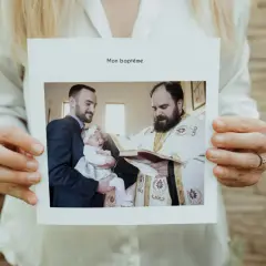 Carte "Mon baptême" tenue par des mains. Photo d'un bébé pleurant, tenu par son père, recevant le baptême d'un prêtre. Un beau texte baptême pour les grands-parents.