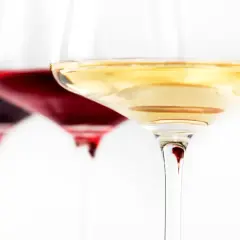 Trzy kieliszki z winem: ciemnoczerwonym, rubinowym i białym. Wino się pieni, tworząc subtelne refleksy.