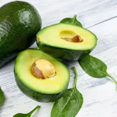 Dwa awokado, jedno całe, drugie przekrojone na pół, leżą na drewnianym blacie. Czy awokado można mrozić?